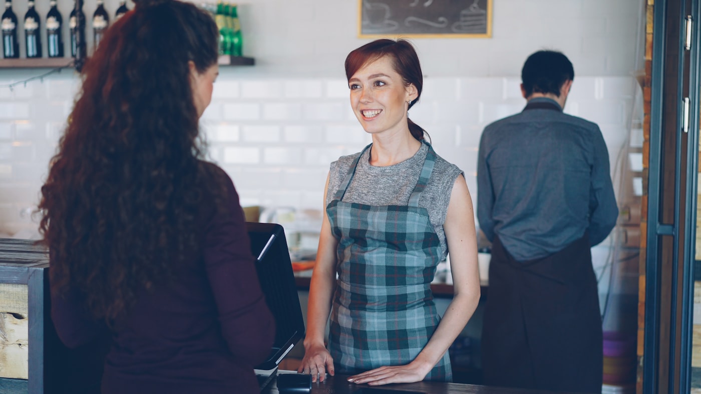 Two people talking warmly across a shop counter
