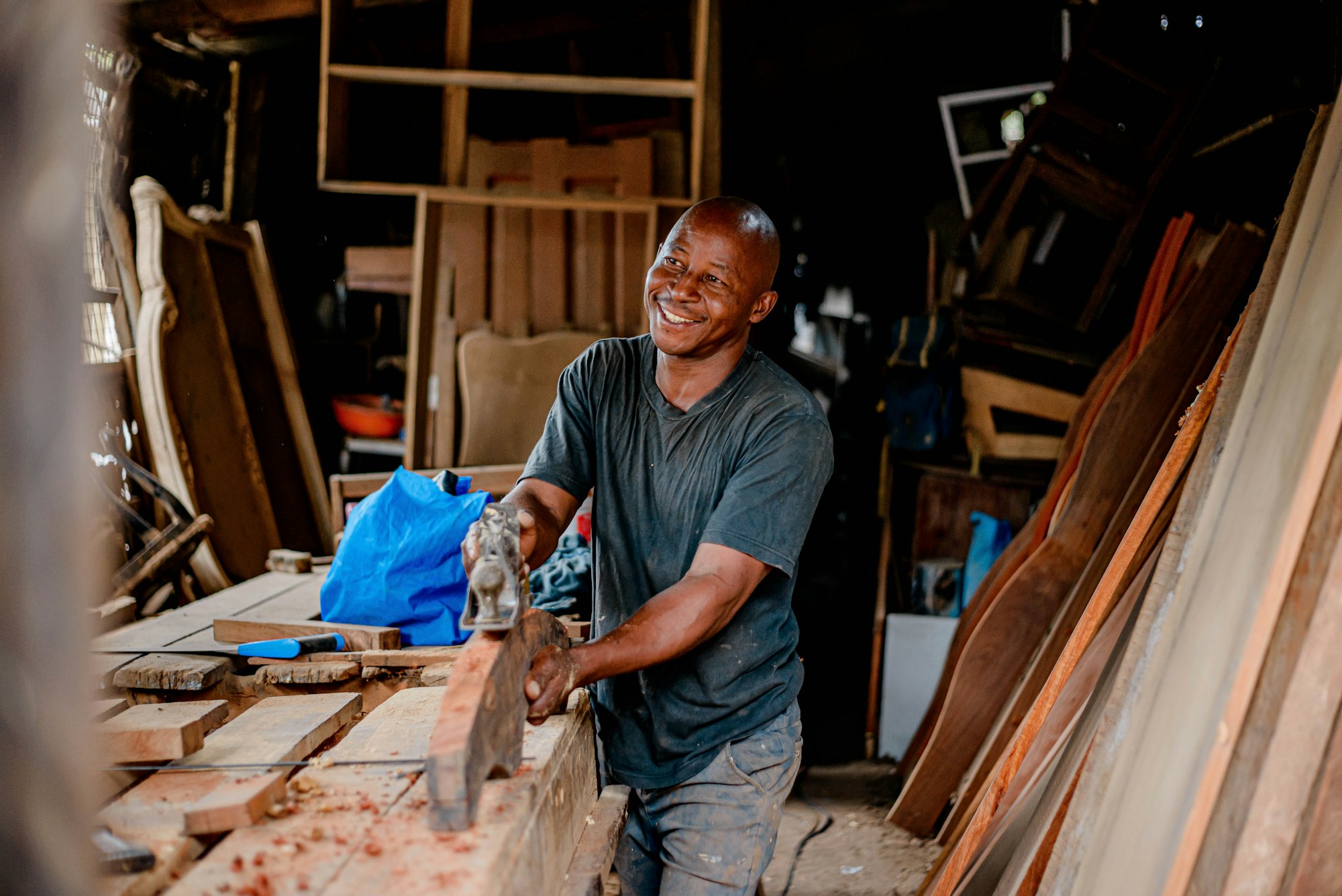 A local craftsman smiling at his workbench, hand-planing a piece of timber in his own workshop